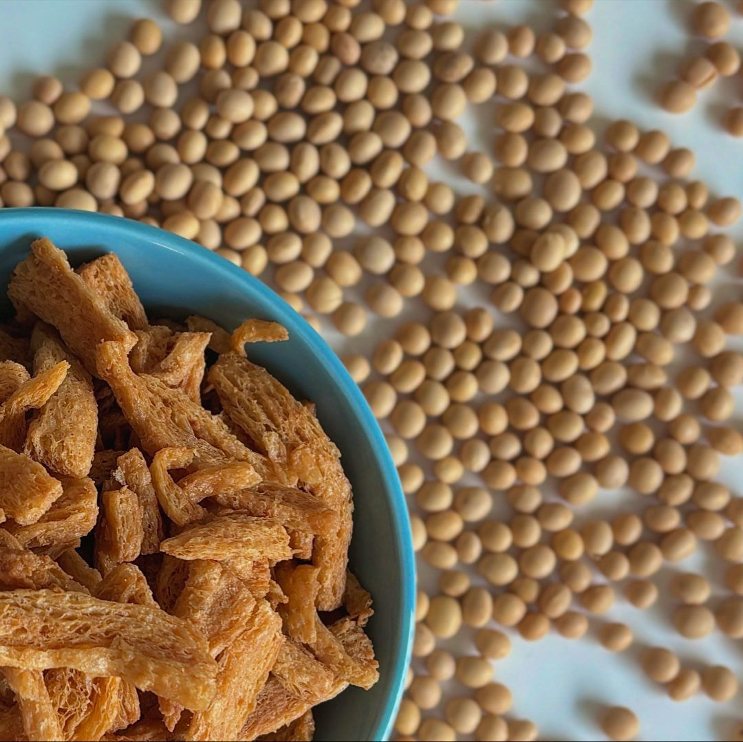 A bowl of tasty soy crunches full of protein, next to a field of delicious soy beans