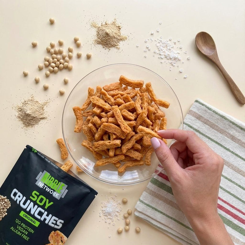 Original Soy Crunches laid out surrounded by fresh soybeans and mushroom powder seasoning, showcasing it as a plant-based soy protein snack from Nibble Network