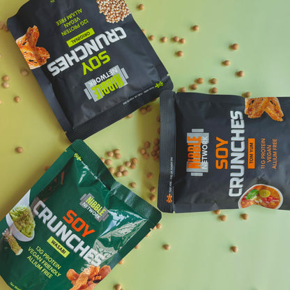 Three packages of Nibble Network Soy Crunches on a green background with scattered soybeans.