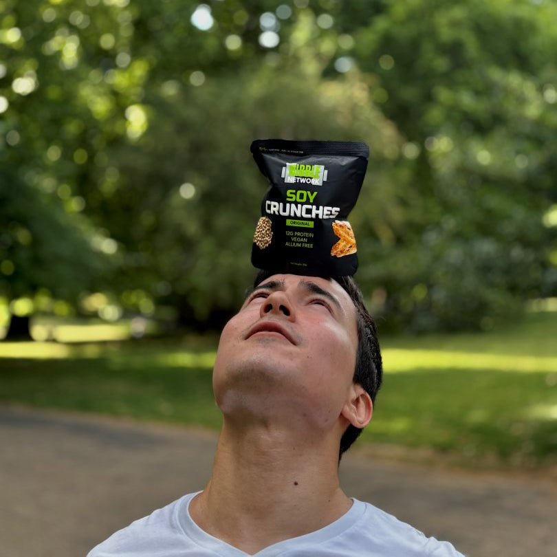 Person balancing a bag of Soy Crunches on their head outdoors with greenery in the background