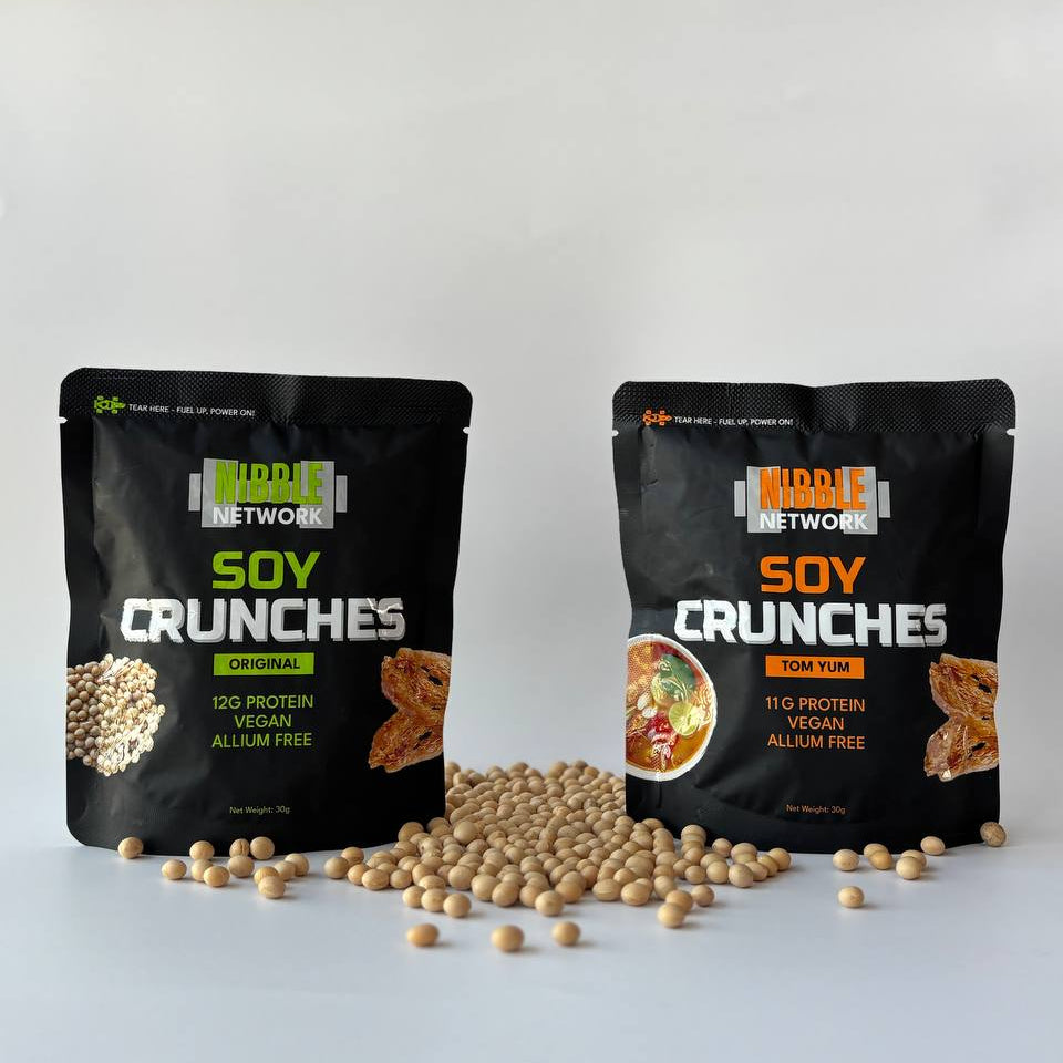 Two packages of Nibble Network soy crunches on awhite background with scattered soybeans surrounding them