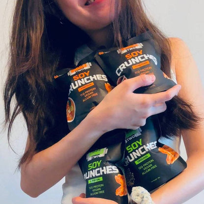 Gwen holding multiple packages of Soy Crunches snack in Original and Tom Yum Nibble Network Soy Crunches, halal-certified allium-free plant protein snacks