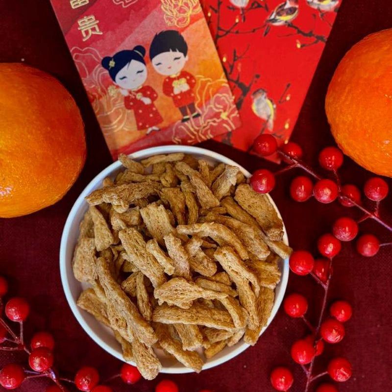 Bowl of Soy Crunches with red envelopes and oranges on a red background, in the spirit of Chinese New Year